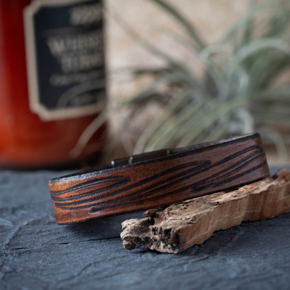 Leather bracelet on a textured surface with a blurred bottle and plant in the background