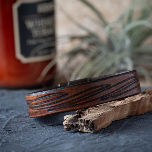 Leather bracelet on a textured surface with a blurred bottle and plant in the background