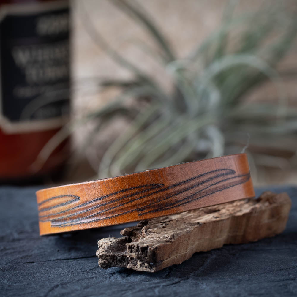 Brown leather cuff with wood grain pattern on a rustic wooden surface