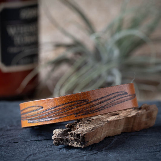 Brown leather cuff with wood grain pattern on a rustic wooden surface