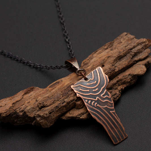 Copper pendant featuring a wood grain texture styledon a piece of wood. 