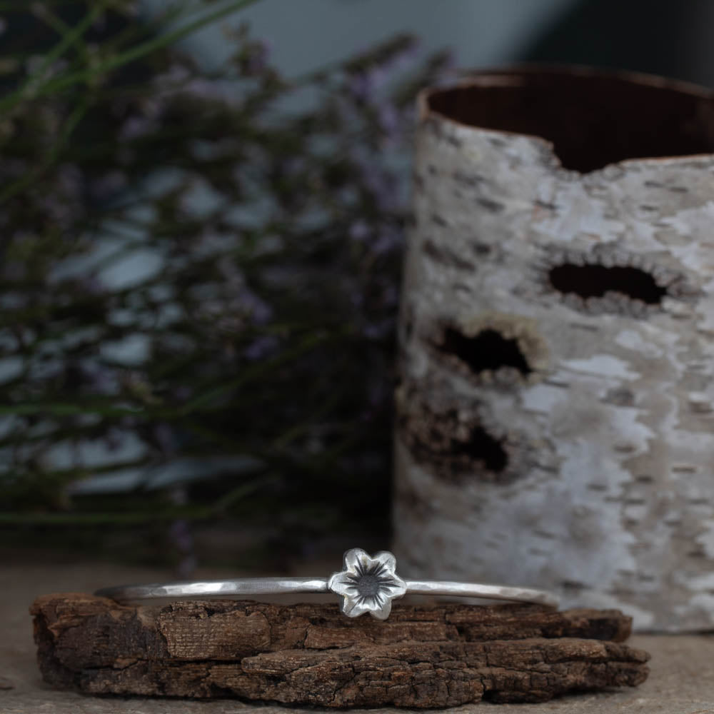 Sterling silver flower bangle bracelet by Divella Designs, handmade in Vermont with smooth satin finish and sculpted blossom on 2 1/2" band, styled with birch bark