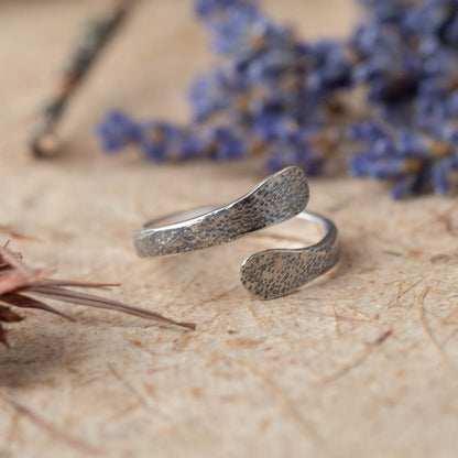 Silver ring with textured surface on a textured surface with blurred purple flowers in the background