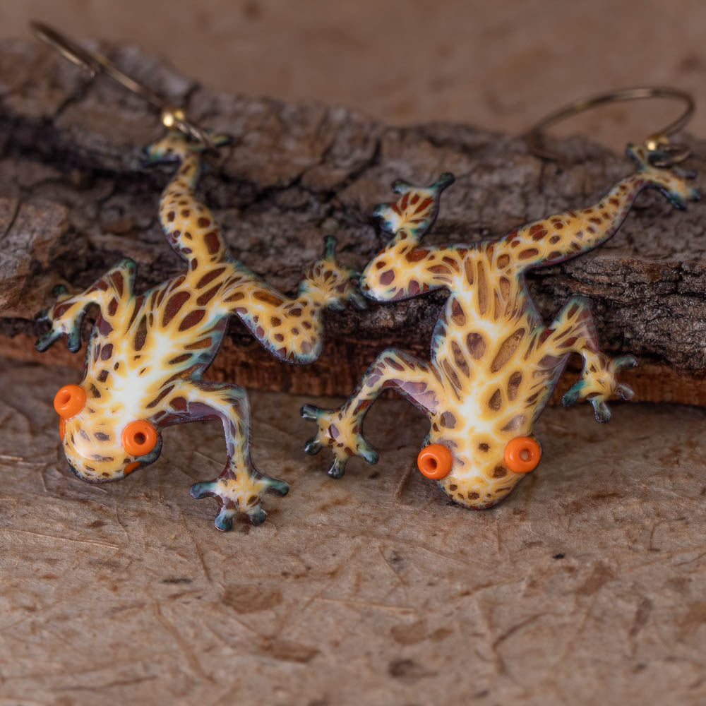Frog-shaped earrings with orange accents on a wooden surface