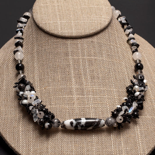 Black and white gemstone necklace featuring zebra jasper, clear quartz, and freshwater pearls in a clustered design, displayed on a neutral linen bust.