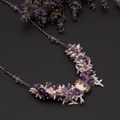 Hand-beaded amethyst and pearl statement necklace with sculptural focal bead, styled on black background with dried lavender flowers