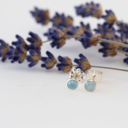 Aquamarine stud earrings set in sterling silver, displayed on a white background with lilac accents.