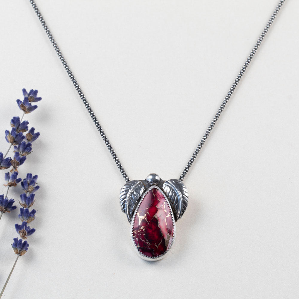 Sterling silver necklace with teardrop dahlia jasper stone in shades of pink and red, accented by two detailed silver leaves and a polished silver bead, handmade botanical jewelry.