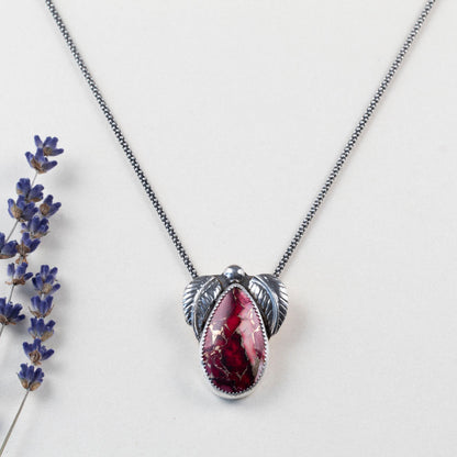 Sterling silver necklace with teardrop dahlia jasper stone in shades of pink and red, accented by two detailed silver leaves and a polished silver bead, handmade botanical jewelry.