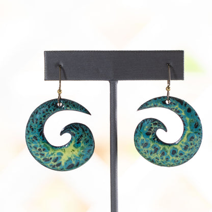 Vibrant spiral enamel earrings in blue, green, and yellow with lichen-inspired texture, handmade with niobium ear wires on a stone background.