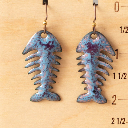 Blue and purple fish bone-shaped earrings on a wooden measuring scale.