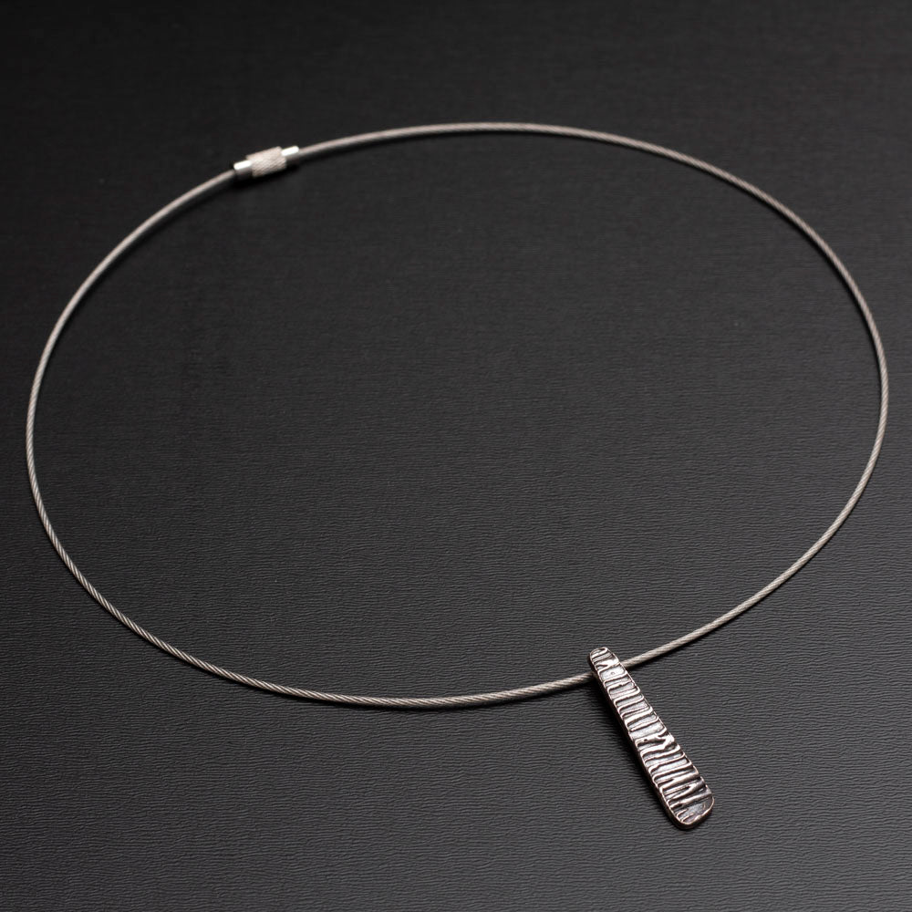 Minimalist silver pendant with tapered shape and organic linear texture on neck wire