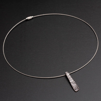 Minimalist silver pendant with tapered shape and organic linear texture on neck wire