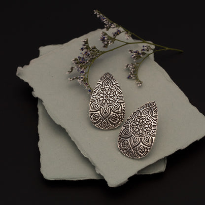 Artisan fine silver teardrop earrings with intricate mandala design, resting on handmade paper with dried lavender and wildflowers – handcrafted by Divella Designs.