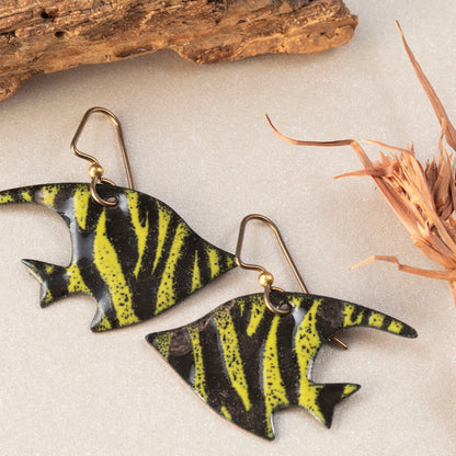 Handmade enamel fish-shaped earrings in bold yellow-green and black stripes, styled with driftwood and natural textures – artisan jewelry by Divella Designs.