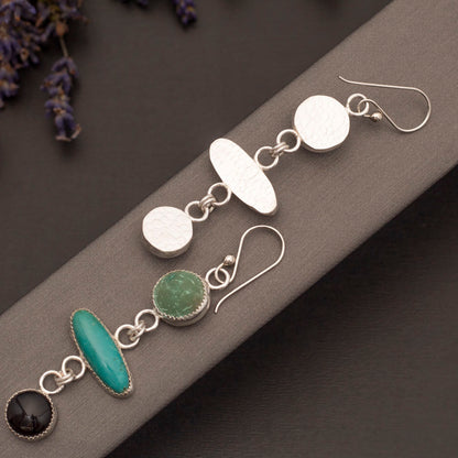 Front and back of Turquoise, Malachite & Onyx earrings pictured on a stand with lilac sprigs peeking out from the side