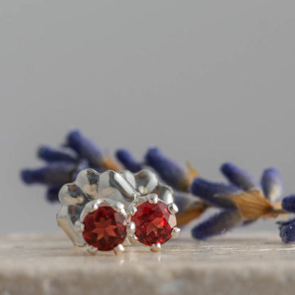 Silver earrings with red garnet gemstones on a tile surface with lavender in the background