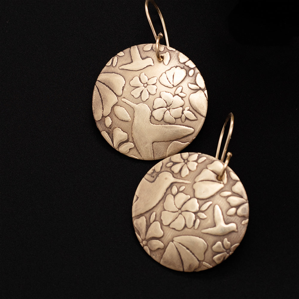 Close up of golden hummingbird earrings on black background.