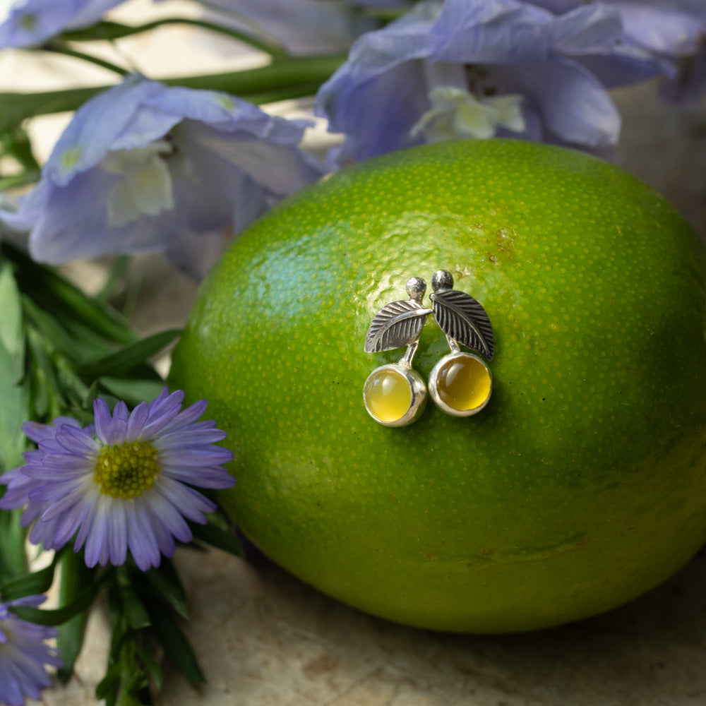 Petite sterling silver Lemon Drop earrings with 6mm yellow chalcedony stones displayed on a green citrus fruit