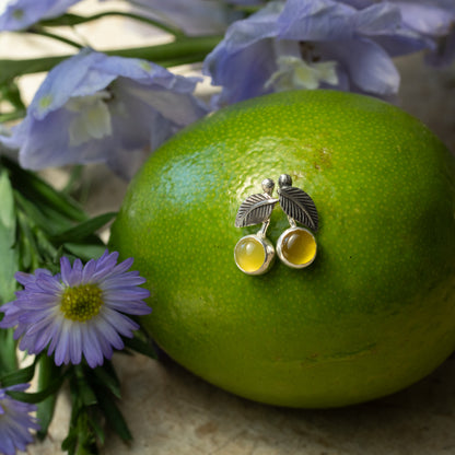 Petite sterling silver Lemon Drop earrings with 6mm yellow chalcedony stones displayed on a green citrus fruit