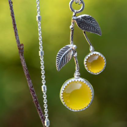 Sterling silver lemon drop necklace with yellow chalcedony stones, textured leaves, and visible silver chain beside a branch.