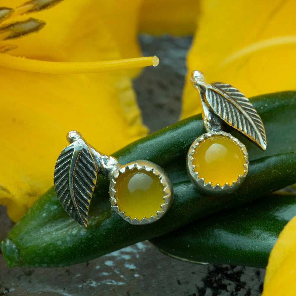 Sterling silver lemon drop stud earrings with yellow chalcedony stones and textured leaves photographed with yellow flowers and green leaves.