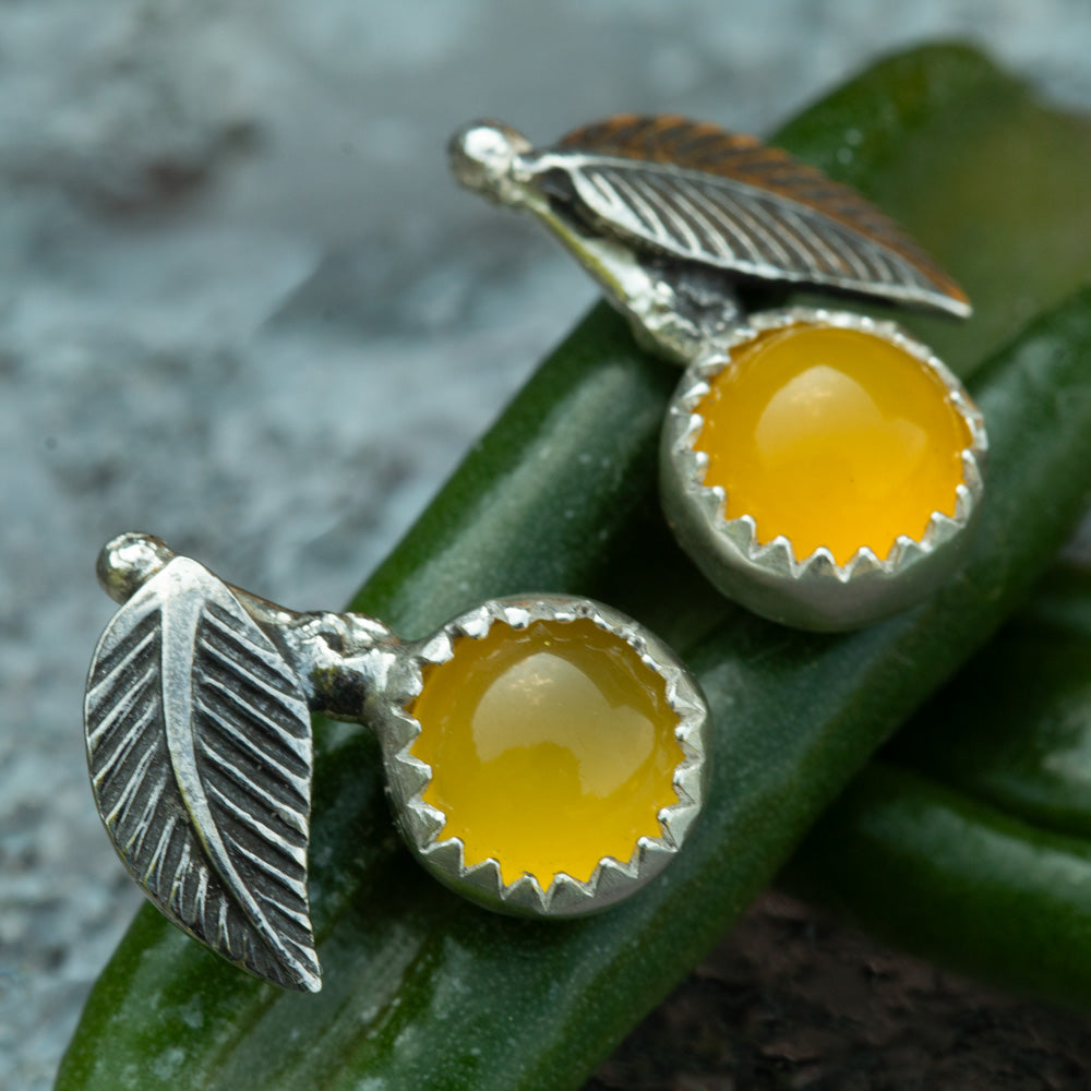 Sterling silver lemon drop stud earrings with yellow chalcedony stones and textured silver leaves resting on green leaves.