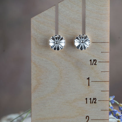Sterling silver flower stud earrings – small hand-crafted floral design with petal texture, polished finish, perfect for everyday wear. Displayed on a wooden ruler for scale.