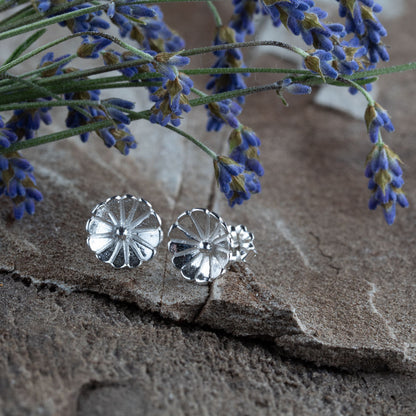 Sterling silver flower stud earrings – small hand-crafted floral design with petal texture, polished finish, perfect for everyday wear. Displayed on natural stone with lavender sprigs.