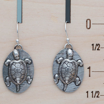 Silver turtle-shaped earrings on a wooden ruler background