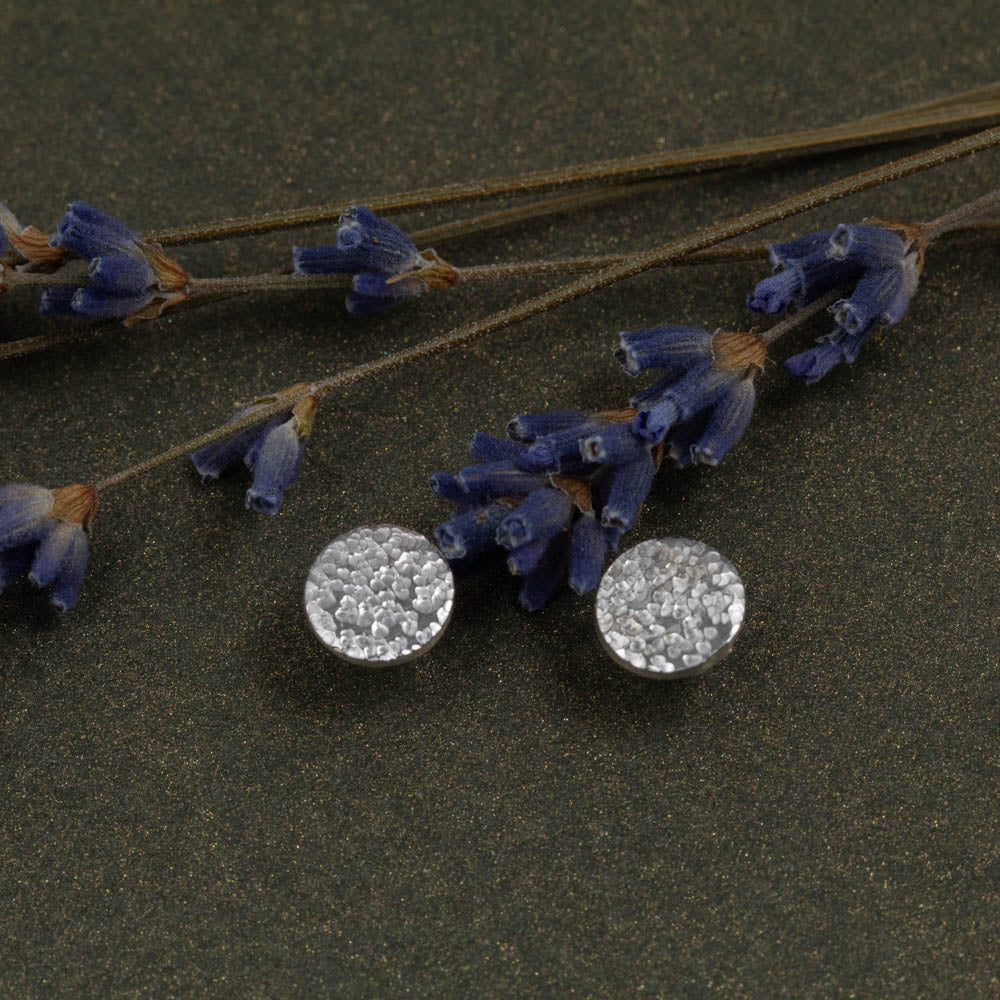 Silver round earrings with floral design on a dark surface with lavender flowers.