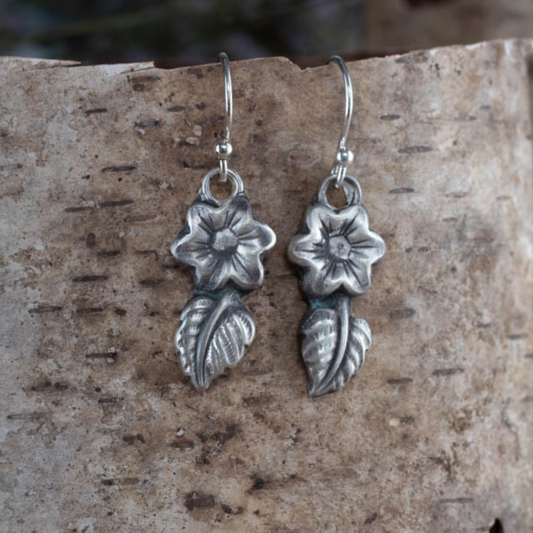 Silver flower-shaped earrings on a textured stone surface