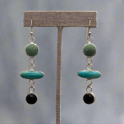 Handmade sterling silver earrings with turquoise, malachite, and onyx gemstones, displayed on a stand with light gray background.