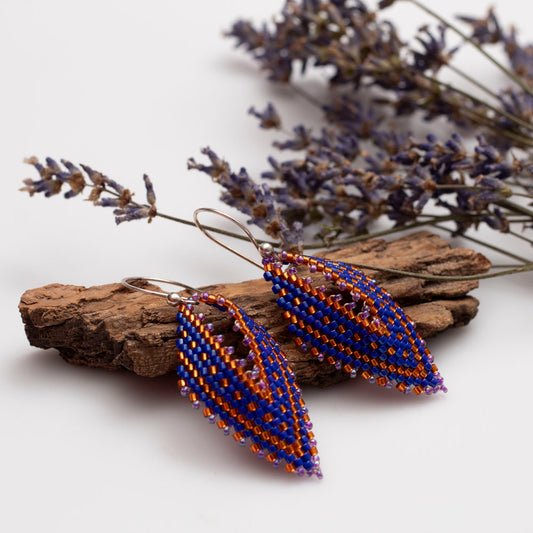 Handwoven orange and blue beaded earrings in a delicate leaf shape, featuring seed beads and metallic accents, handmade by Divella Designs.