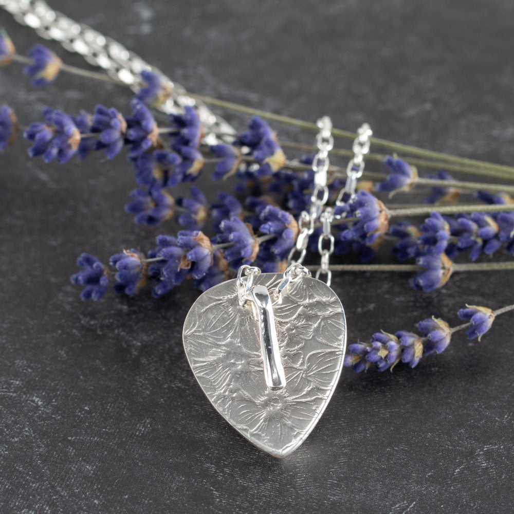Back view of handcrafted sterling silver pendant with floral texture and custom bail, displayed with dried lavender on dark stone background – artisan jewelry by Divella Designs