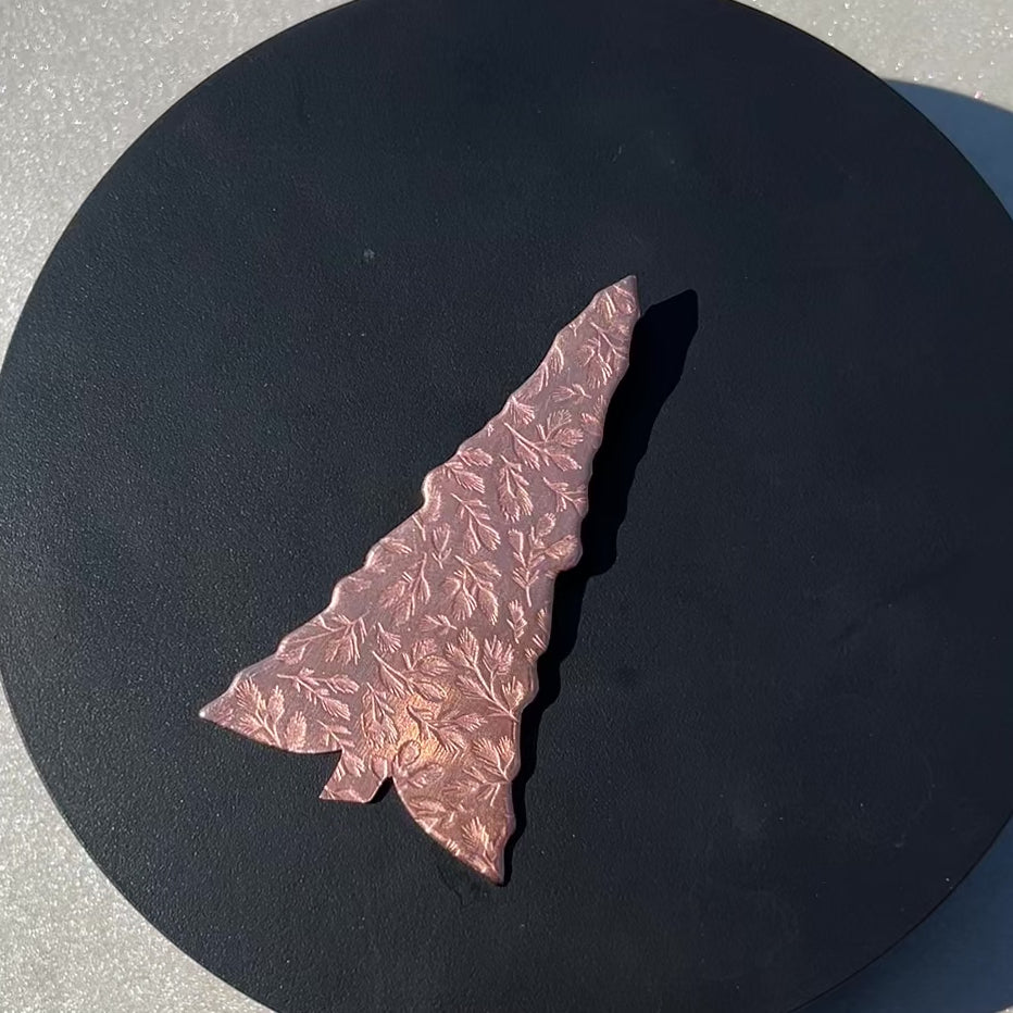 Tree shaped Copper ornament with pine branch texture on a black surface