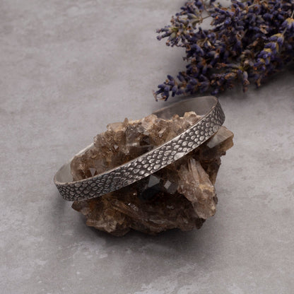 Sterling silver cuff bracelet with a raindrop texture, displayed on an amethyst crystal with lilac sprigs on the background.