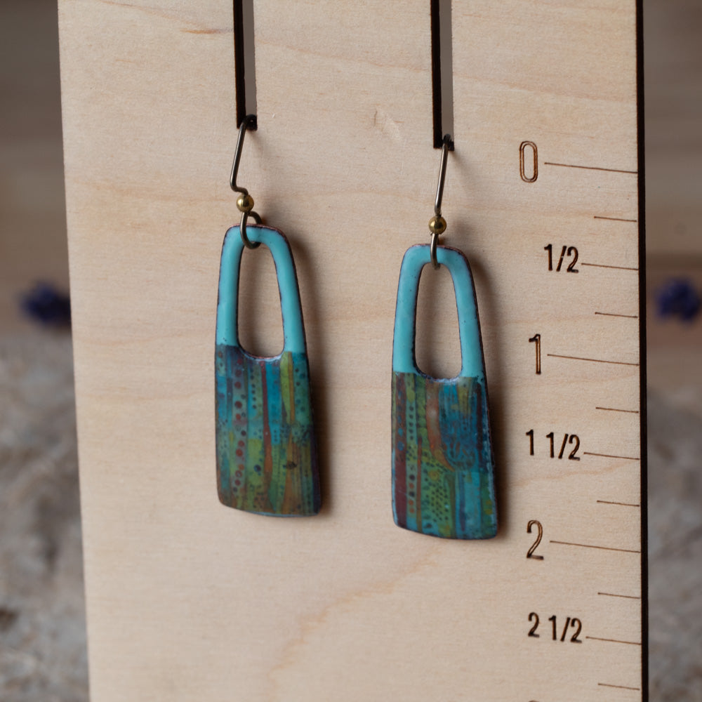 Blue rectangular enamel earrings with open cutouts, turquoise tops, striped earthy details, and niobium ear wires.