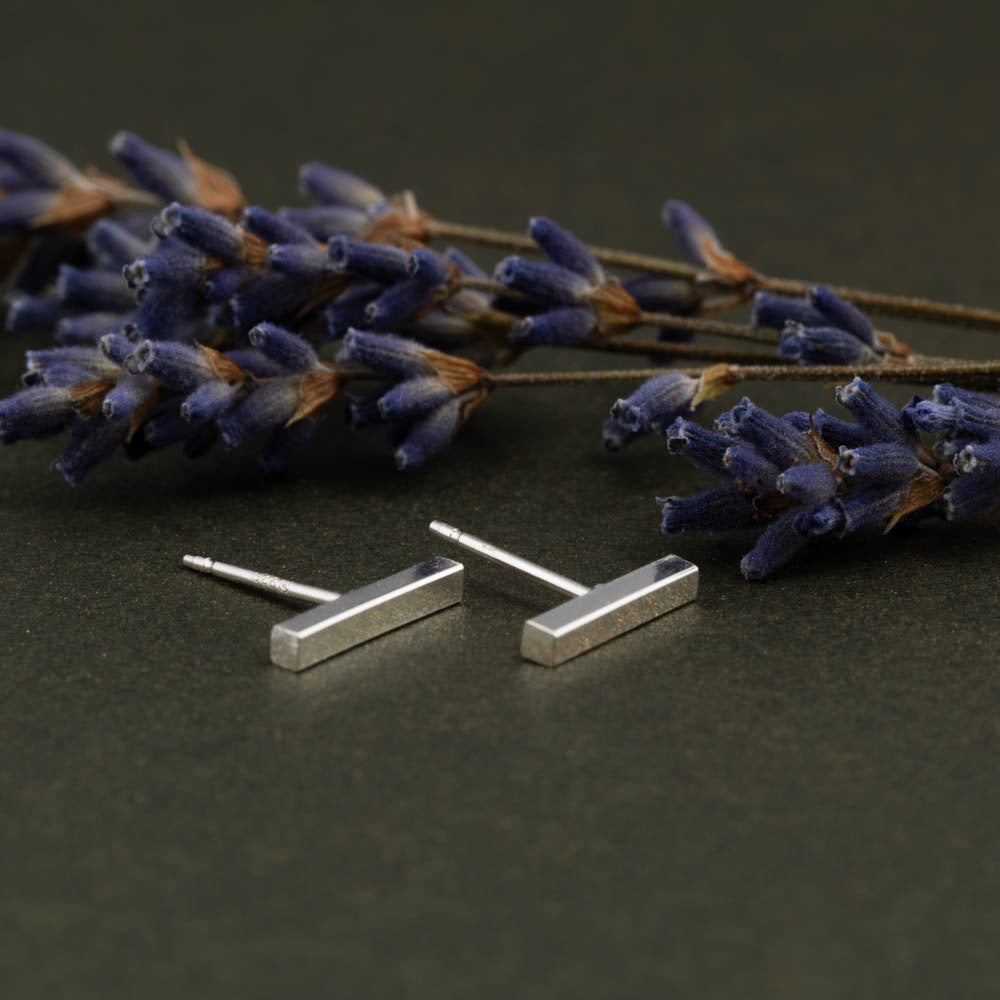 Silver bar earrings on a dark surface with lavender flowers