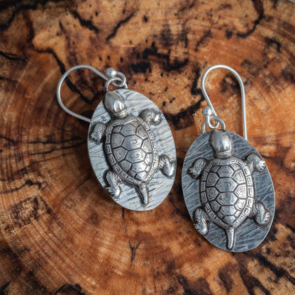Silver turtle earrings on a wooden surface
