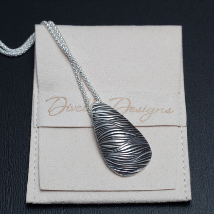 Handmade sterling silver necklace with teardrop pendant featuring a flowing wave texture, modern artisan design on a sterling popcorn chain. pictured on branded pouch.