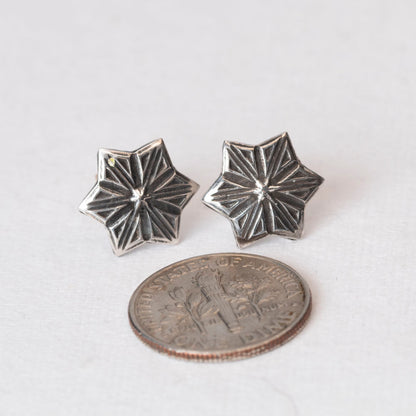 Pair of handcrafted sterling silver star-shaped stud earrings with etched radiating lines, displayed on a light fabric backgroun