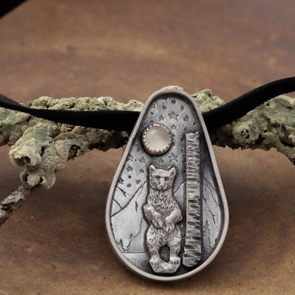 Sterling silver bear and moonstone pendant on black leather lace with woodland background