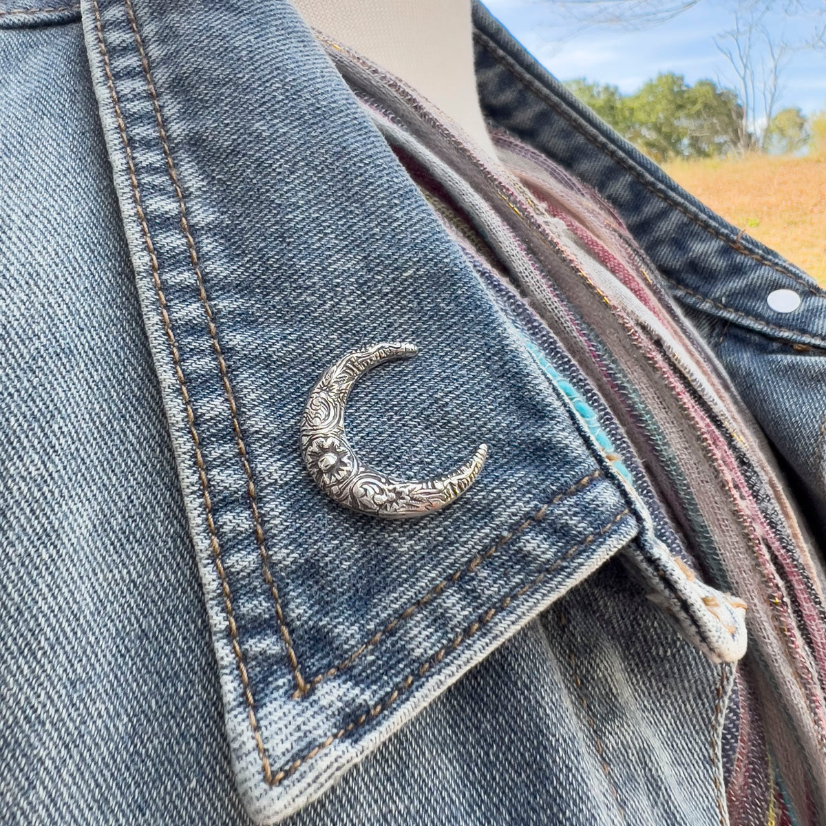 Denim jacket with a decorative silver crescent moon pin on a blurred outdoor background