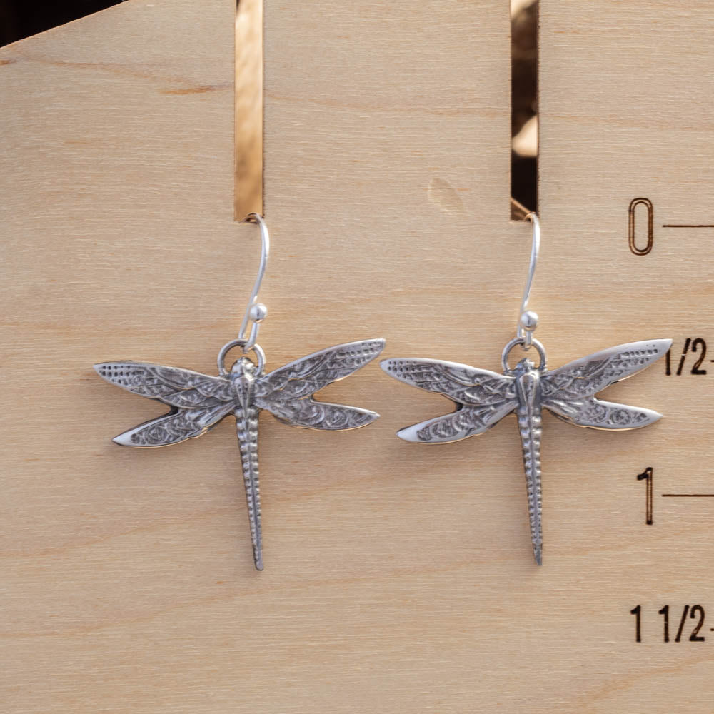 Silver dragonfly earrings on a wooden ruler for scale.