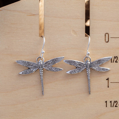 Silver dragonfly earrings on a wooden ruler for scale.