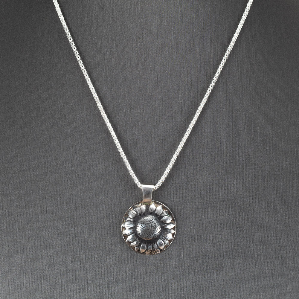 Handcrafted sterling silver sunflower pendant with oxidized details for depth and texture, hanging on a shimmering chain – artisan floral necklace by Divella Designs