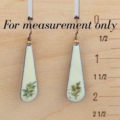 Teardrop-shaped earrings with floral design on a wooden ruler background