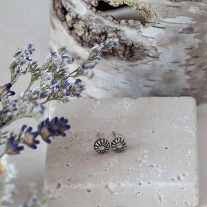 Tiny handmade sterling silver stud earrings with oxidized floral sunburst design, featuring 5mm round shape and minimalist vintage-inspired style. Pictured on travertine block.
