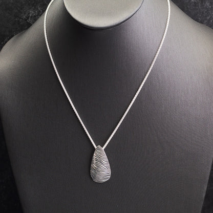Handmade sterling silver necklace with teardrop pendant featuring a flowing wave texture, modern artisan design on a sterling popcorn chain.